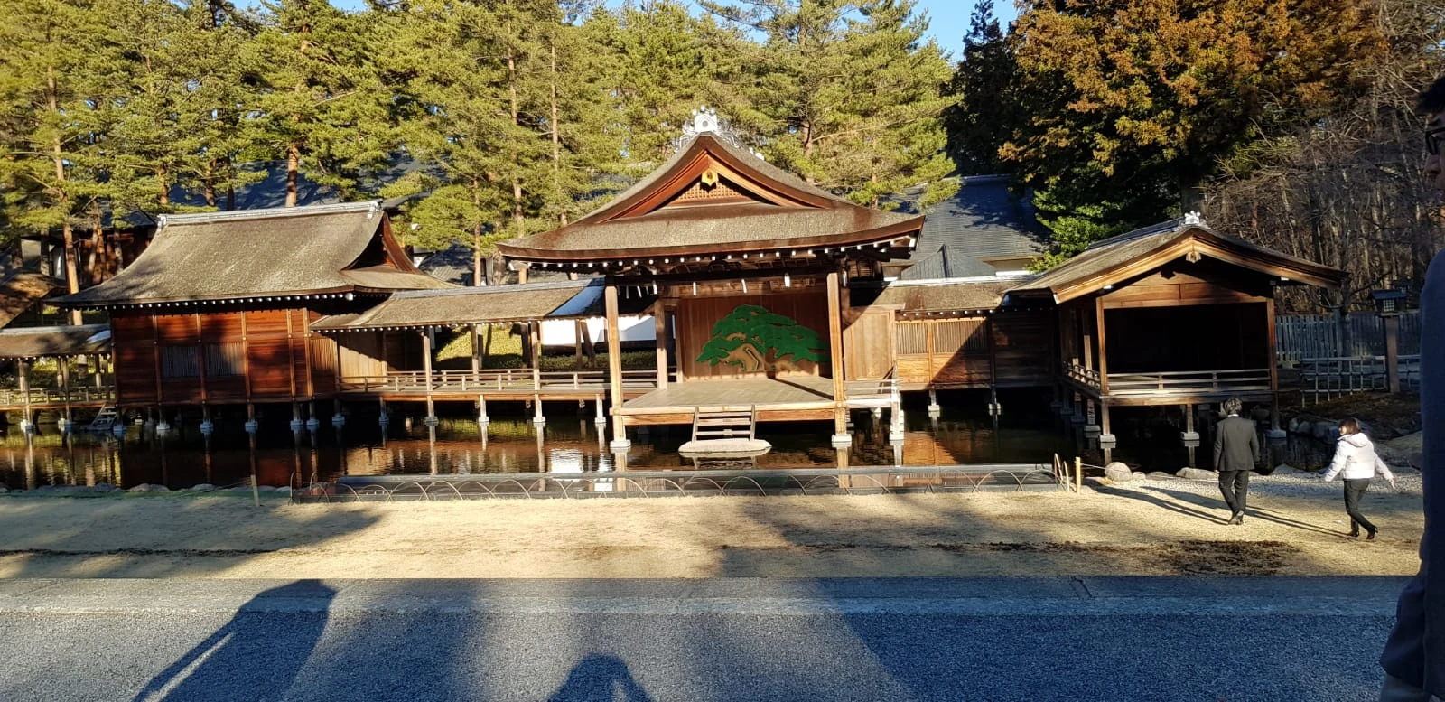 A traditional shrine and its forecourt framed by tall trees.