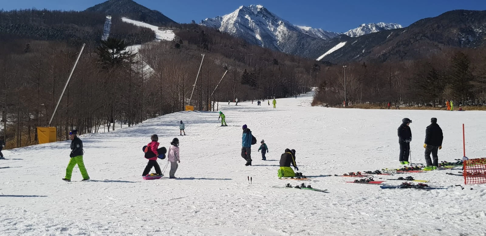 Skiers on a snowy slope below rugged mountain peaks and a blue sky.