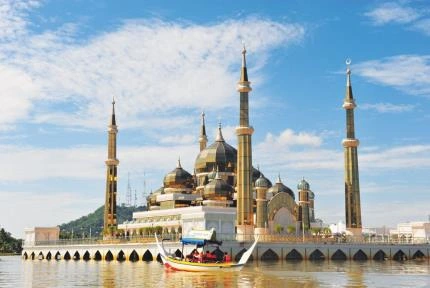 An ornate mosque with tall minarets and golden domes beside the water.