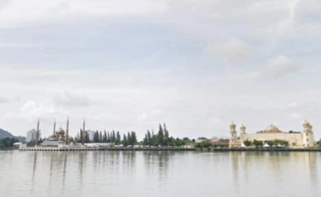 A wide waterside view of a mosque and its minarets beneath a cloudy sky.